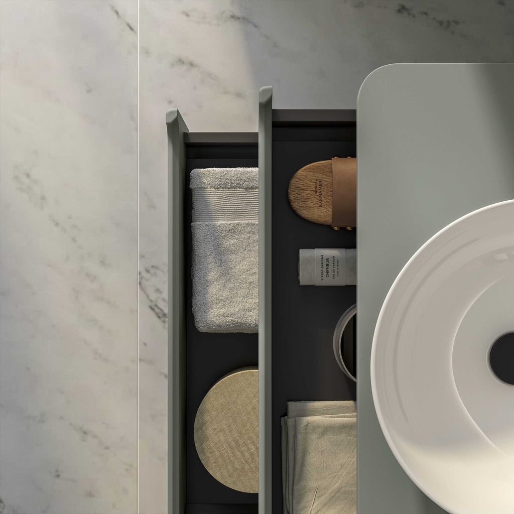 Luxurious bathroom accessories including a white towel, bamboo soap dish, skincare products, and beige cloth on a sleek dark grey side table with a modern white sink.