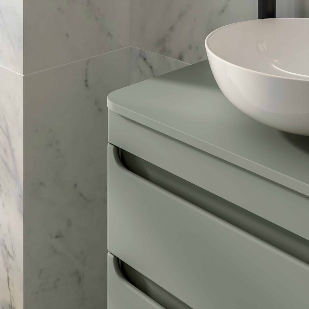 Sleek modern bathroom vanity with a white vessel sink, minimalist design, soft muted green colour, against a marble tiled wall, showcasing stylish and functional bathroom furniture from Bubly Bathrooms.