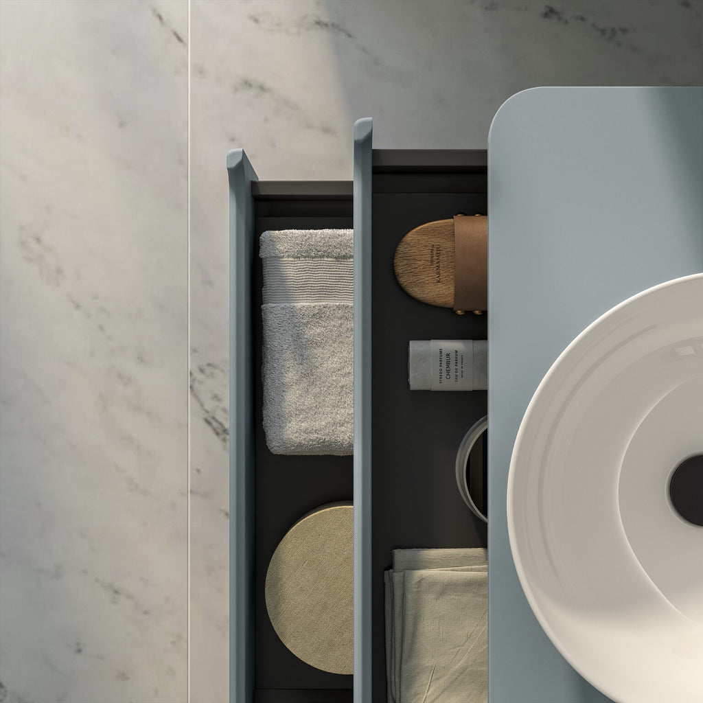 Minimalist bathroom storage with neatly organised towels, toiletries, and accessories on a sleek grey cabinet under a modern white basin.