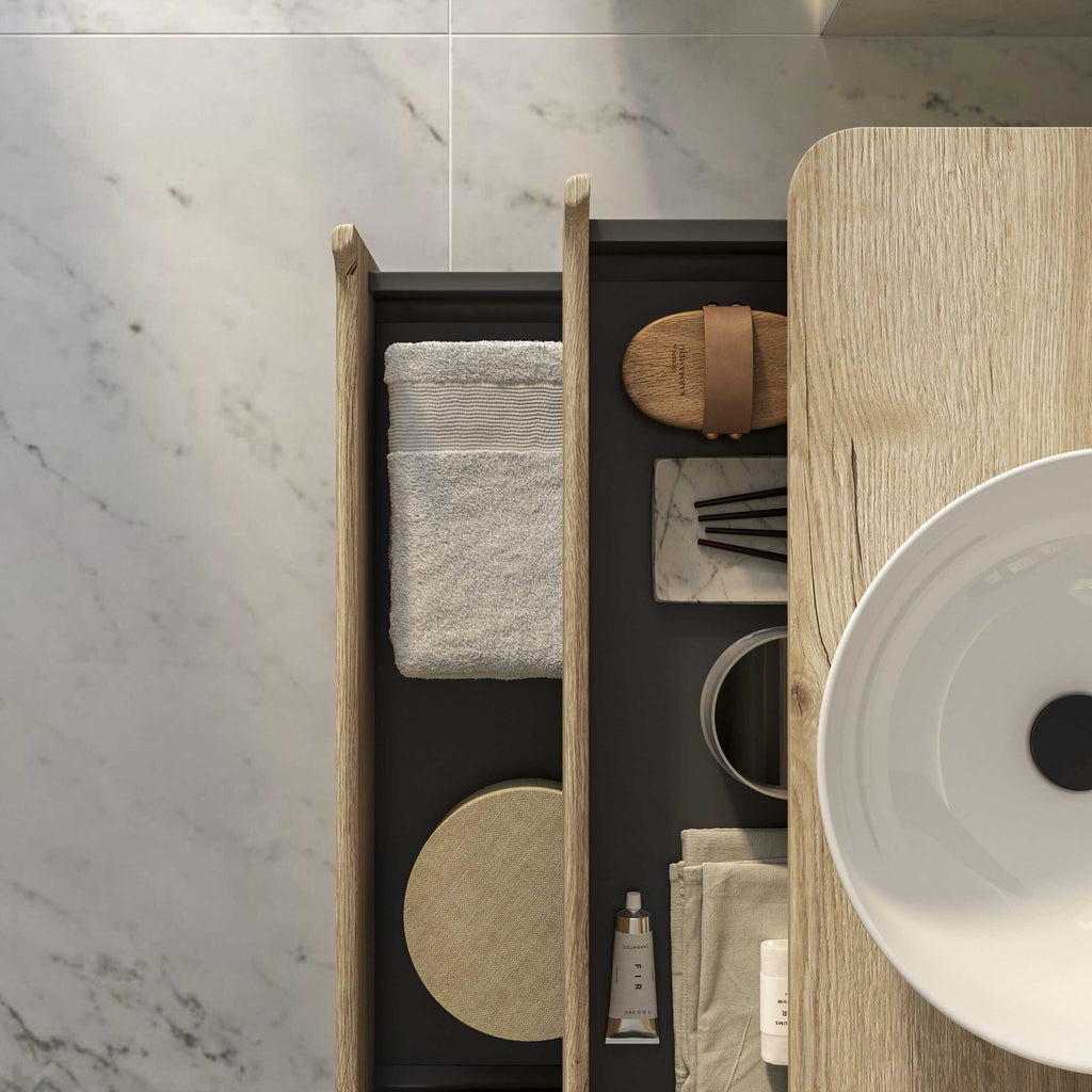 Stylish bathroom vanity with wooden accents, open storage drawers containing towel, decorative marble tray, skincare products, and accessories on a marble floor, creating an elegant and modern bathroom space.