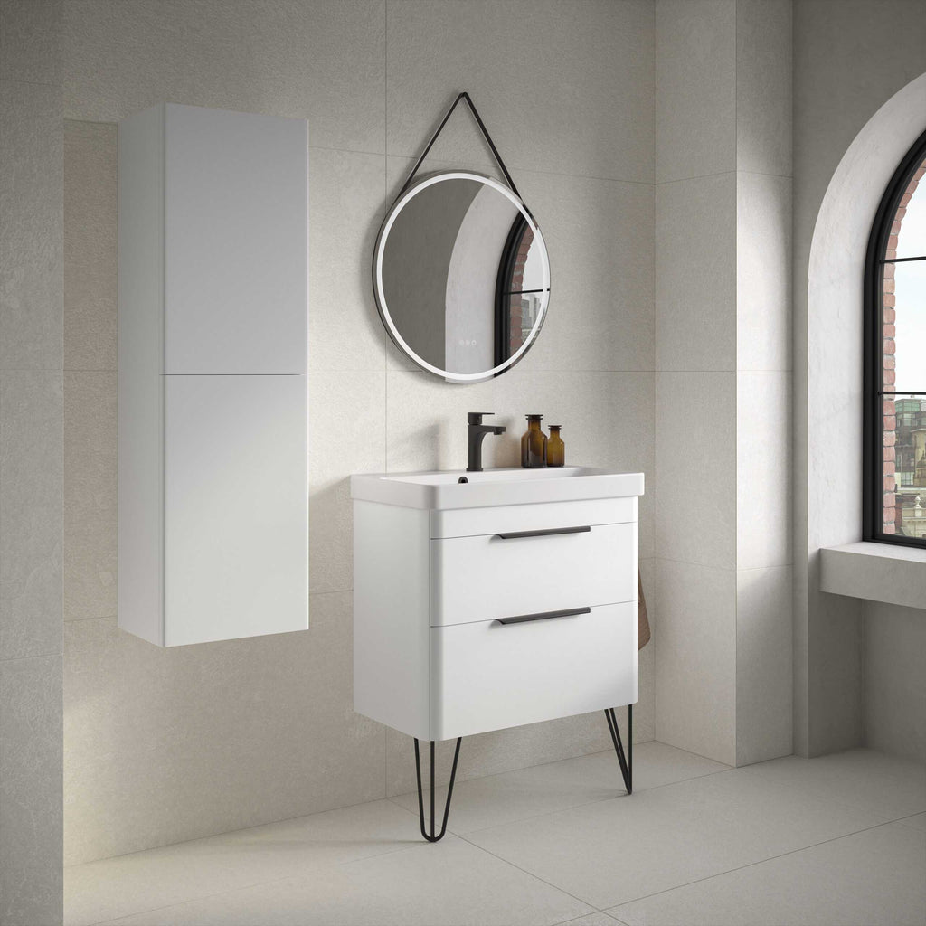 Modern white bathroom vanity unit with black handles and hairpin legs, paired with a circular mirror and wall storage cabinet, in a minimalist bathroom with neutral tones and large arched window.