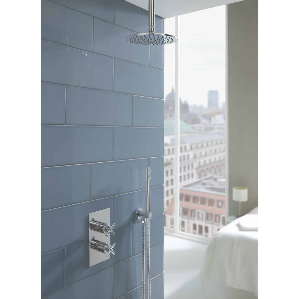Shower fixtures with rain shower head and modern chrome controls in a contemporary bathroom with blue wall tiles and a cityscape view.