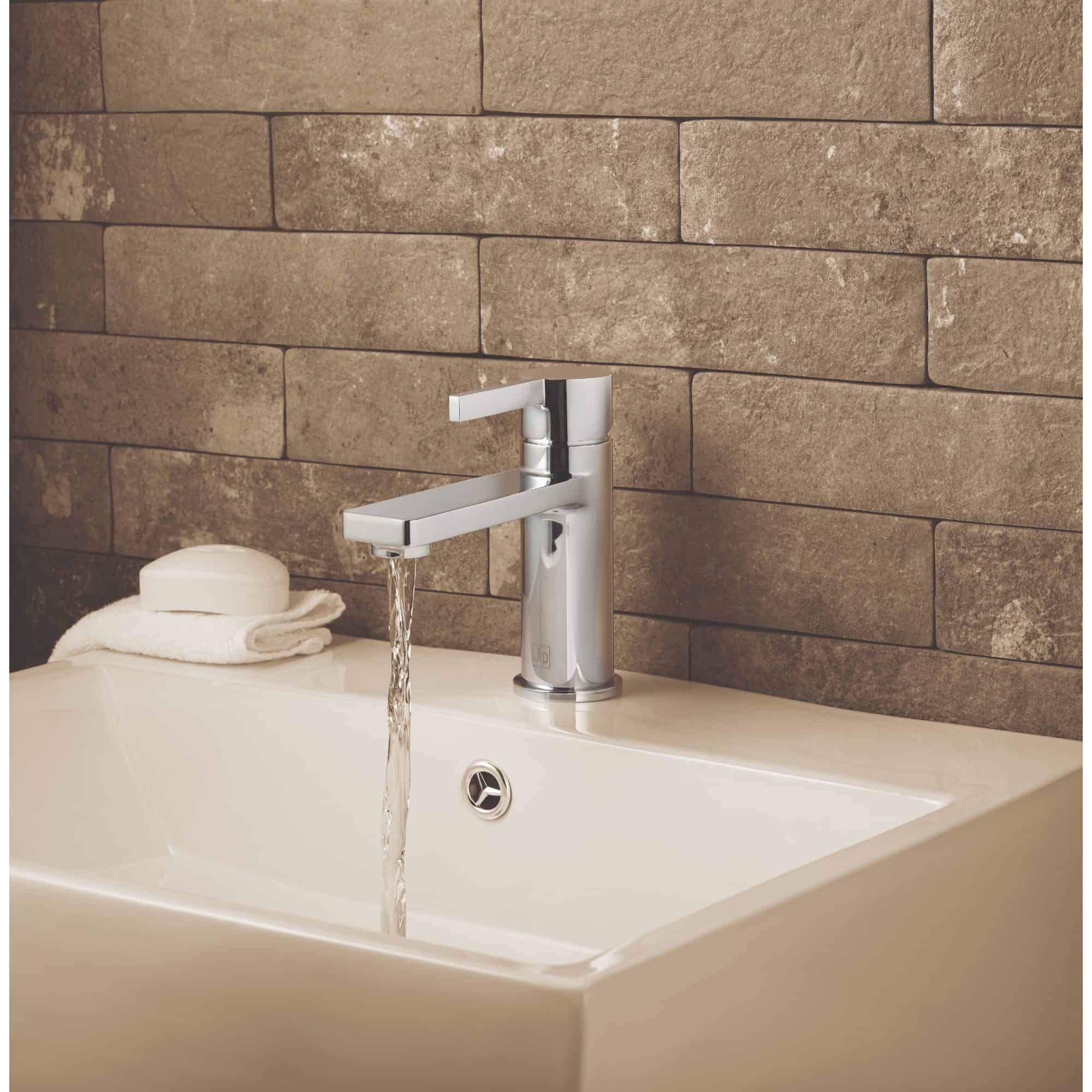 Sleek modern bathroom sink with a chrome faucet, a white towel, and soap, set against a textured brown brick wall, showcasing high-quality bathroom fixtures from Bubly Bathrooms.