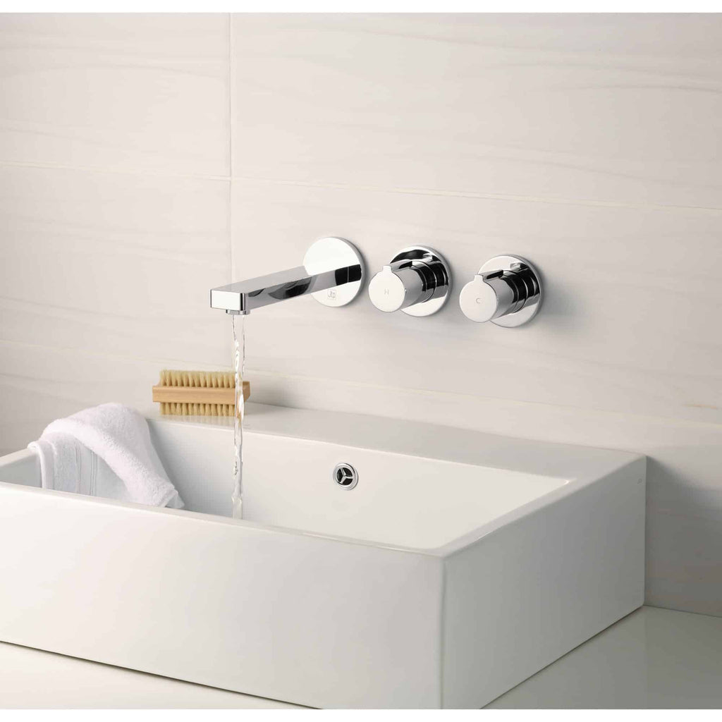 Chrome tap with wall-mounted control knobs for modern bathroom sink, elegant minimalist design, shiny chrome finish, integrated with white ceramic basin, featuring towel and bath brush detail for bath fixtures SEO.