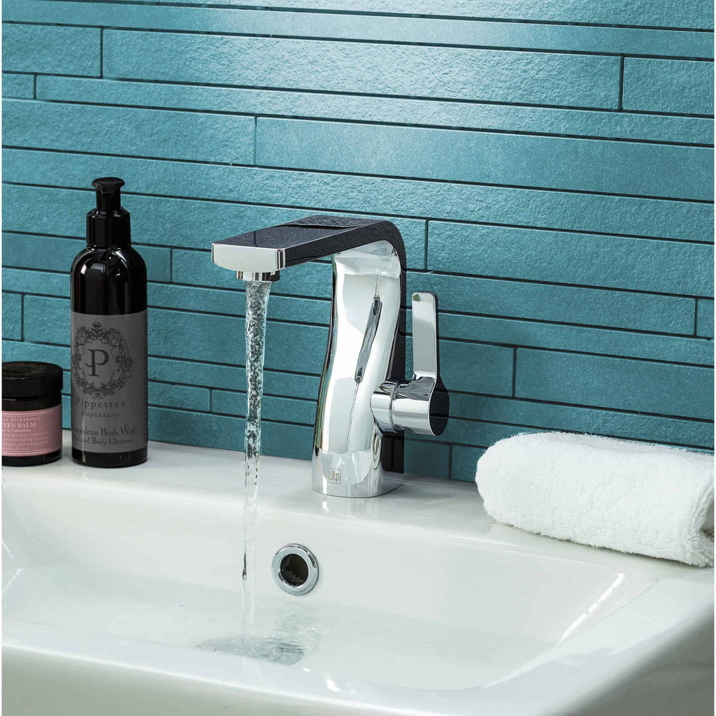 Shiny chrome bathroom tap with flowing water, set against a textured turquoise tiled wall, with personal care items and a neatly rolled white towel nearby.