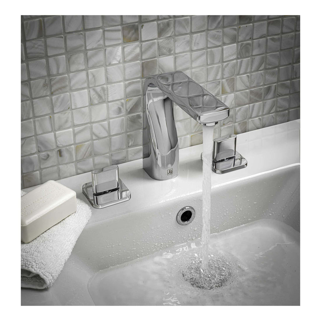 Shiny chrome bathroom mixer tap with a modern design, mounted on a white sink with water flowing, against a backdrop of stylish grey mosaic tiles.