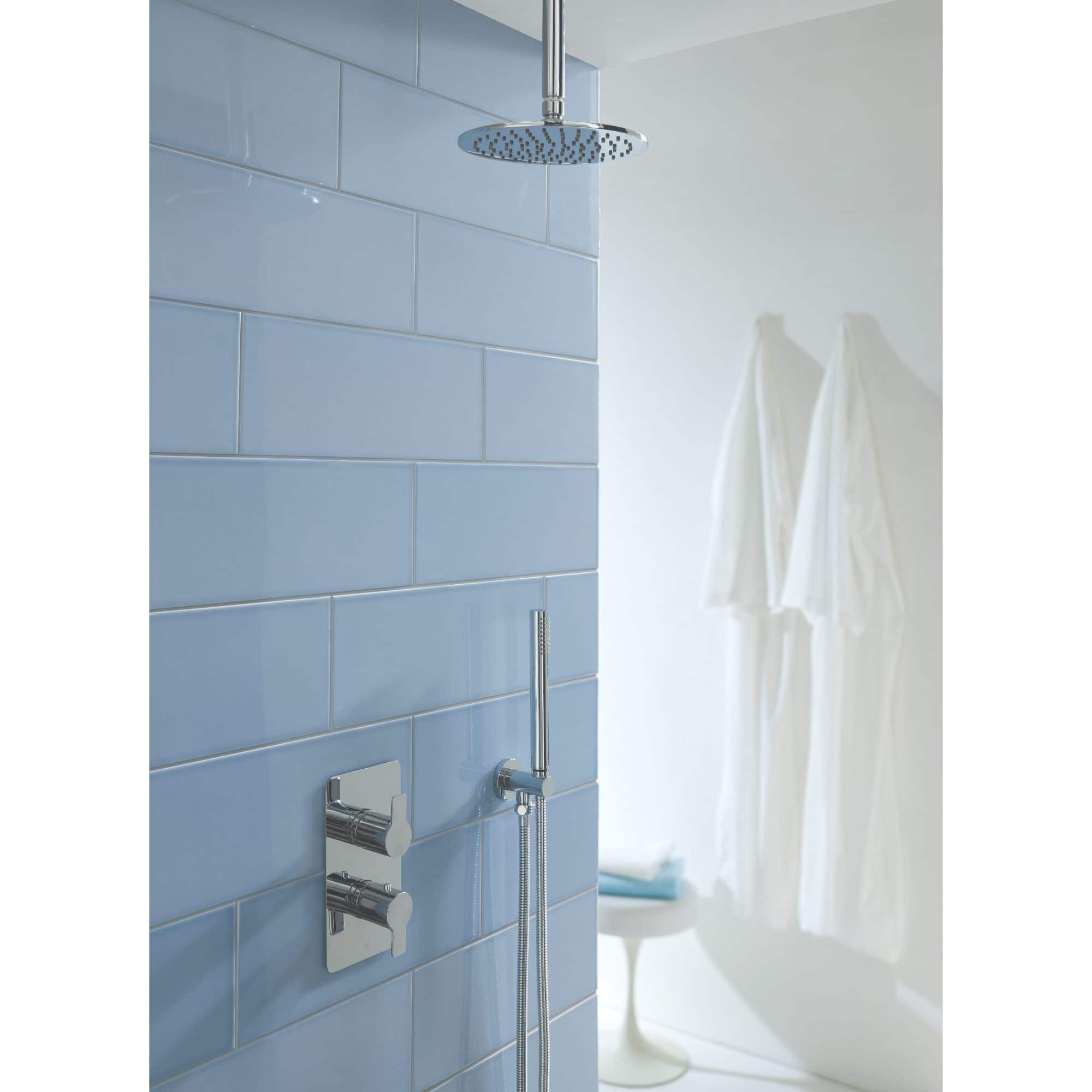 Modern rain shower head and chrome fixtures in blue tiled bathroom.