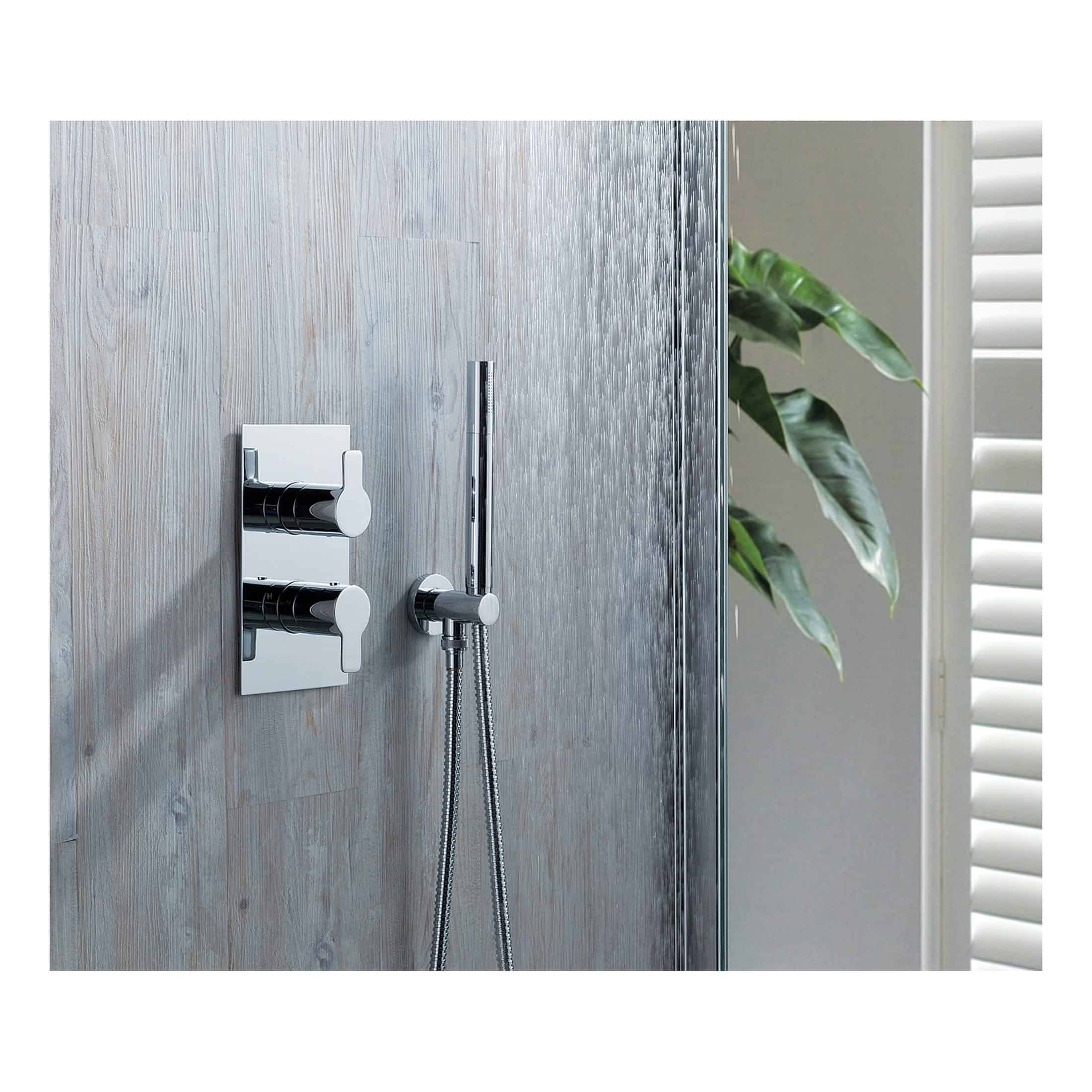 Sleek modern chrome bathroom shower mixer with handheld shower head, mounted on stylish textured wall with a green plant and white shutters in the background.