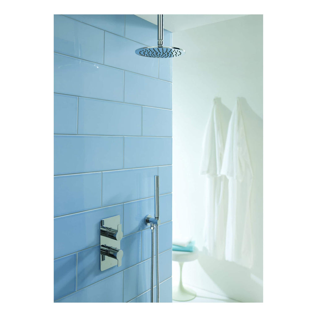 Polished chrome showerhead and controls on a blue tiled bathroom wall with white towels in the background.