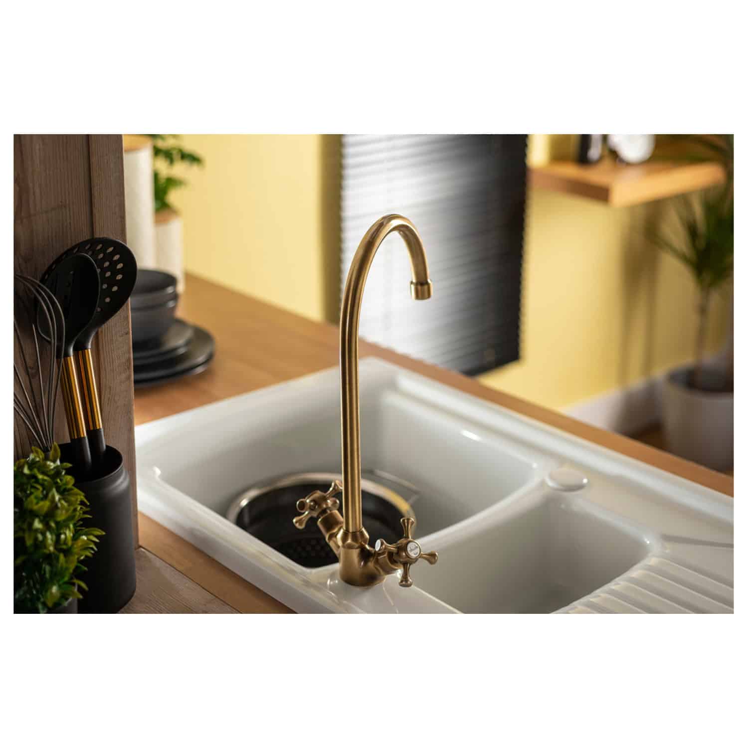 Shiny gold kitchen sink tap with traditional cross handles, installed in a white ceramic sink with drainer, in a modern kitchen setting, showcasing stylish and functional bathroom and kitchen fixtures.