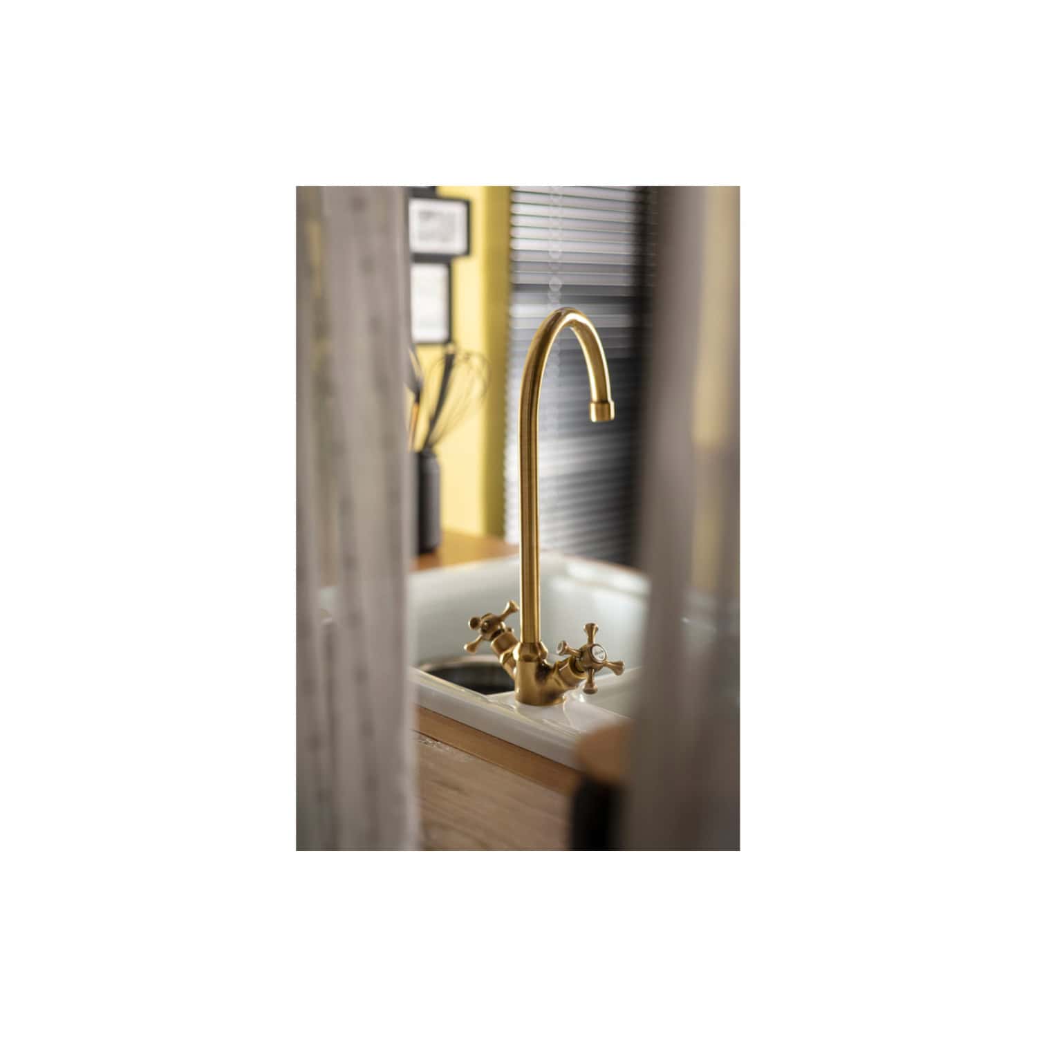 Shiny gold kitchen faucet mounted on a white sink with a wooden countertop, modern bathroom design with window blinds, elegant plumbing fixture for stylish bathrooms, premium quality bath accessories, luxurious kitchen sink tap installation.