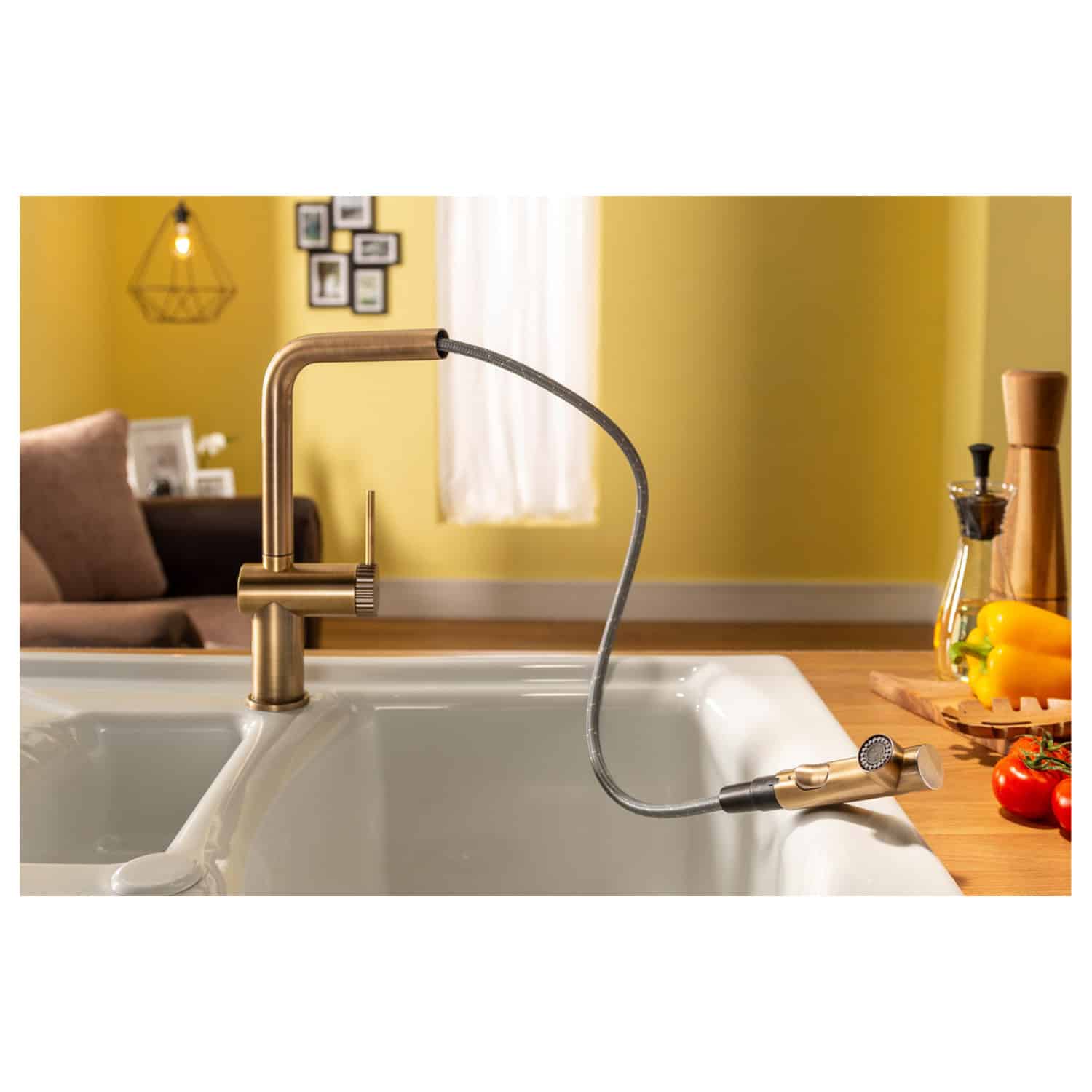 Sleek modern kitchen sink with a stylish gold faucet and pull-out spray head in a contemporary home setting. Bright yellow walls, decorative accessories, and fresh vegetables complement the functional design.