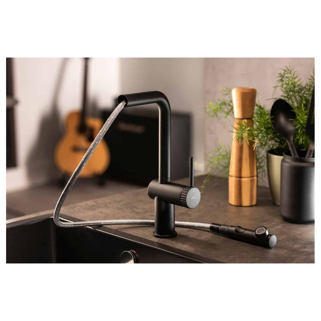 Sleek black kitchen faucet with pull-down spray head, modern design, and matte finish, installed on a dark countertop, surrounded by indoor plants, wooden pepper mill, and kitchen utensils, perfect for contemporary bathroom or kitchen upgrade.