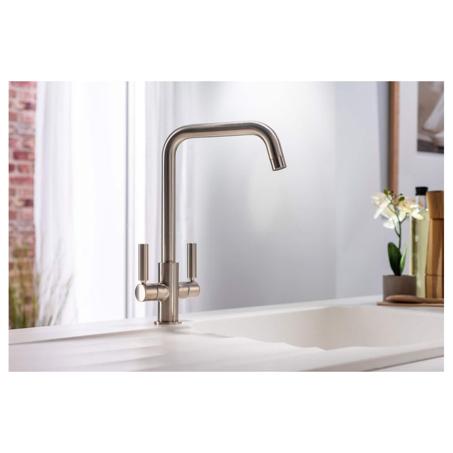 Polished stainless steel kitchen faucet with modern design, high-arc spout, and dual handles, installed on a white kitchen sink in a contemporary kitchen setting.