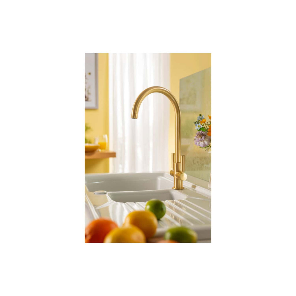 Shiny gold kitchen tap above a white sink in bright, modern kitchen with yellow walls and fresh fruit on the counter, showcasing luxury bathroom and kitchen fixtures by Bubly Bathrooms.