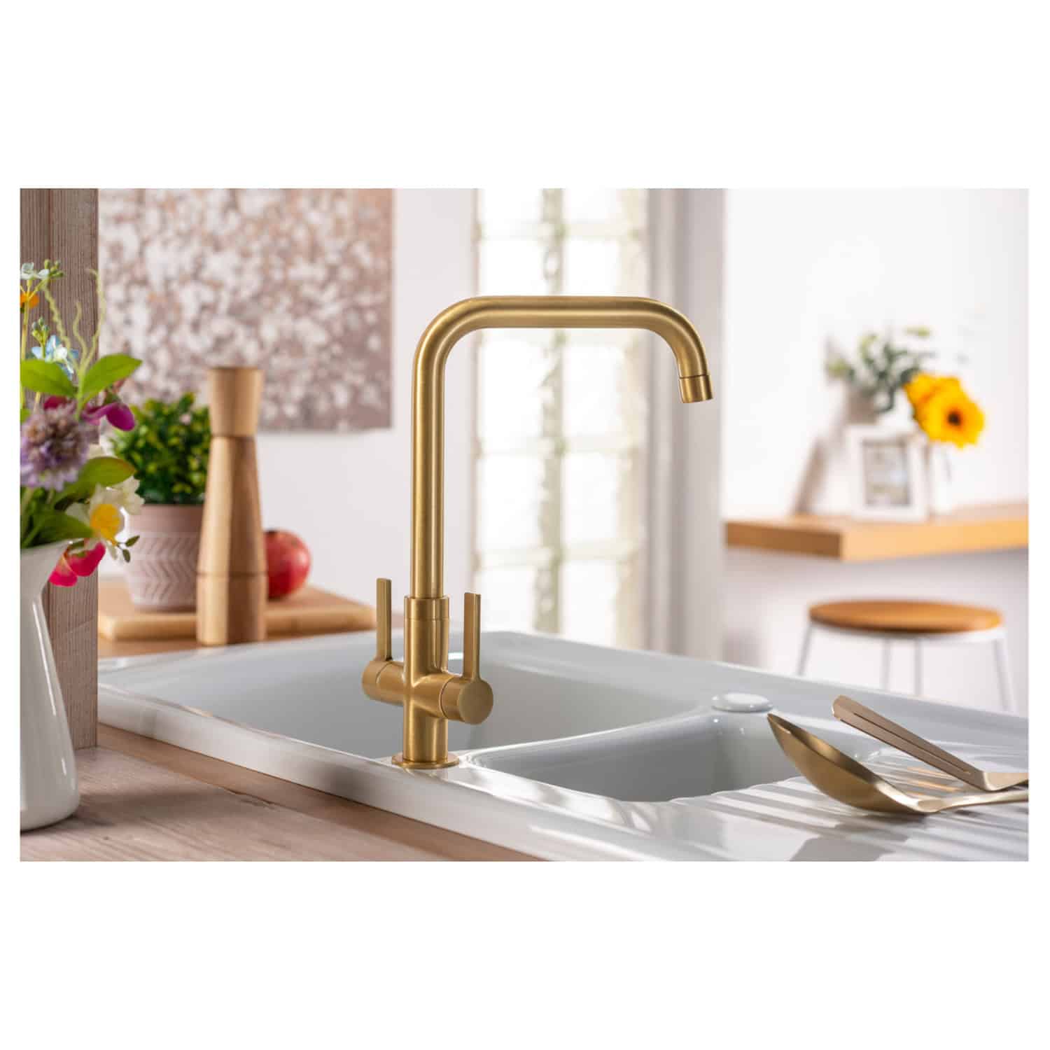 Shiny gold kitchen sink tap with modern design in a contemporary kitchen setting, featuring a white sink, wooden accents, and decorative flowers for a stylish and functional kitchen upgrade.