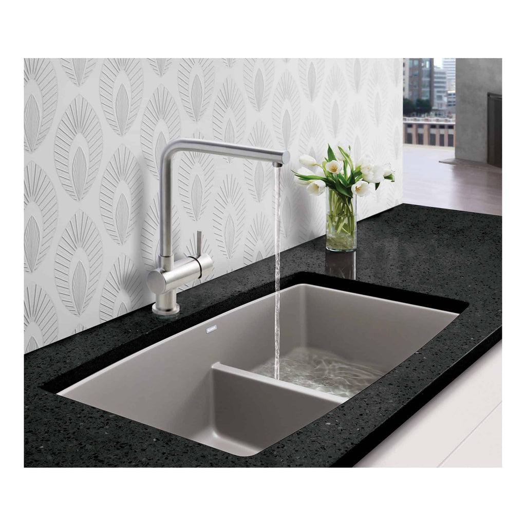 Stainless steel kitchen sink with modern tap and black granite countertop, decorated with a vase of white tulips against patterned white wallpaper.