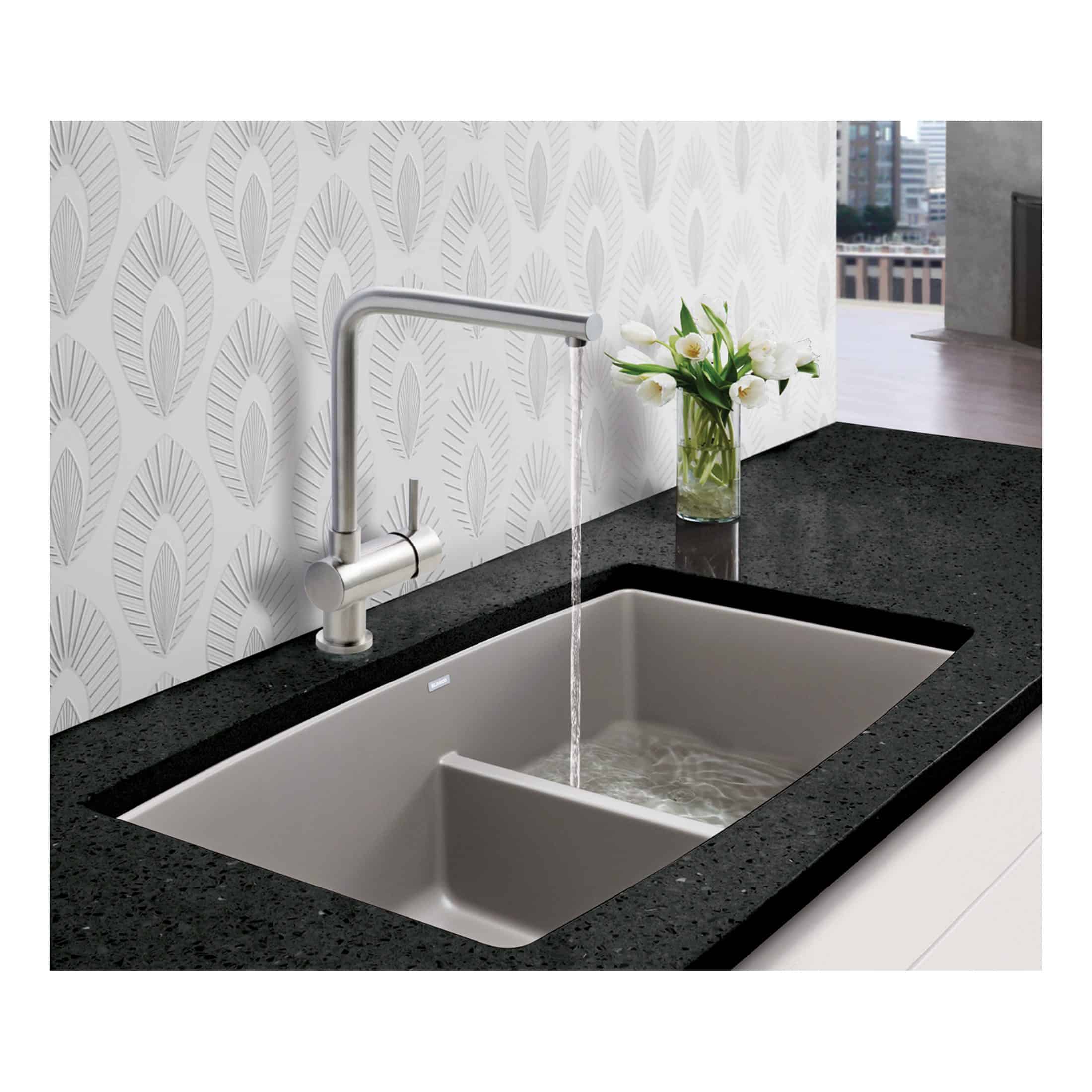 Stainless steel kitchen sink with modern tap and black granite countertop, decorated with a vase of white tulips against patterned white wallpaper.