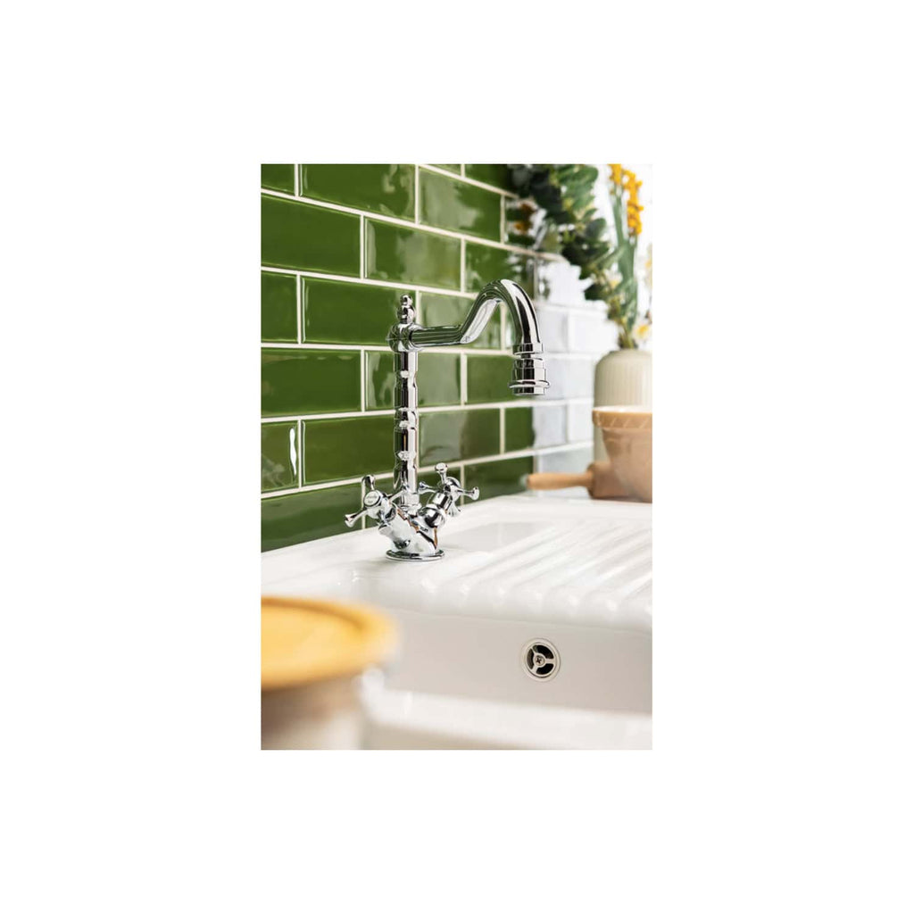 Shiny chrome kitchen sink faucet with vintage design, mounted on a white ceramic sink with drainer, set against a vibrant green tiled backsplash in a modern bathroom or kitchen.
