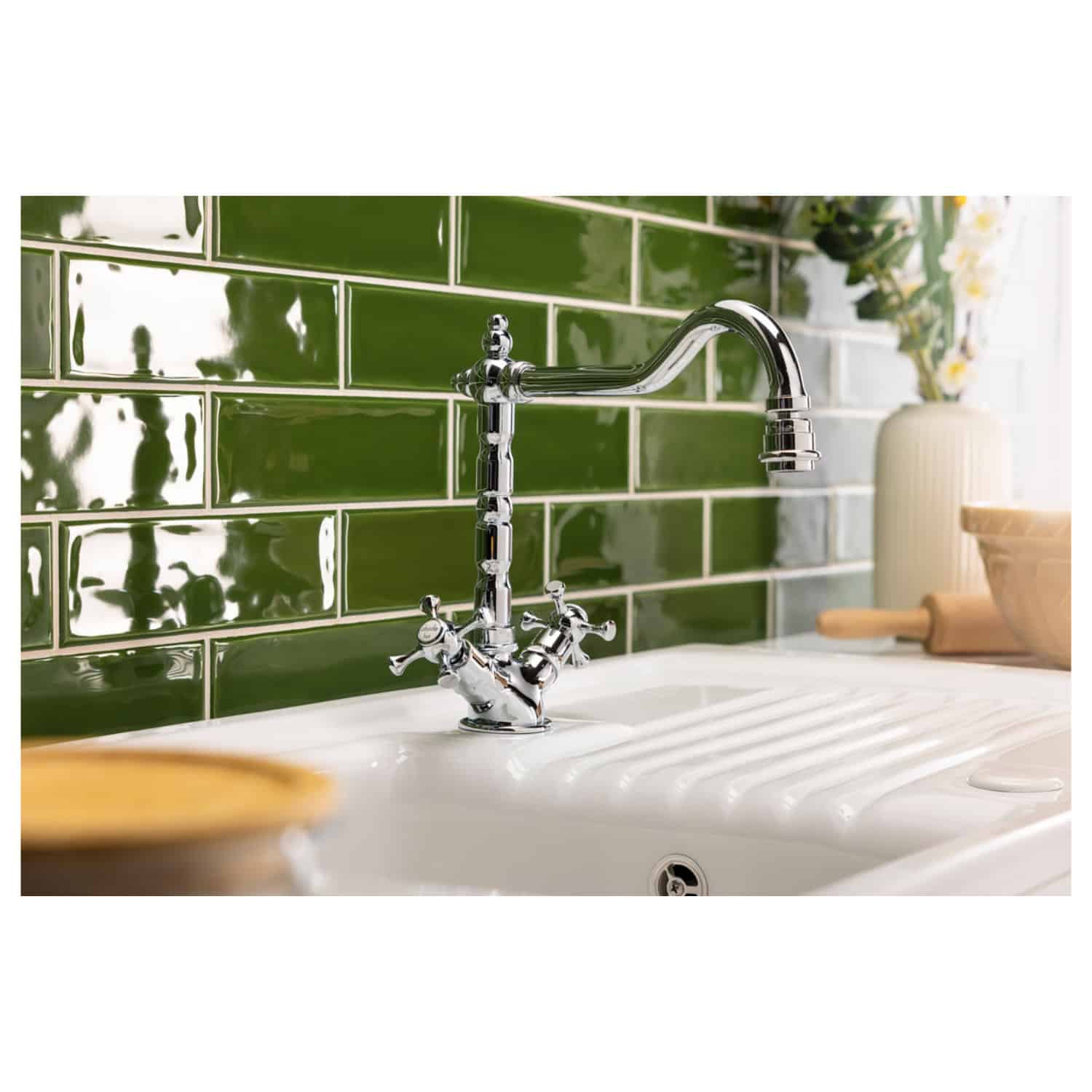 Sleek chrome kitchen faucet with vintage-inspired handles installed on a white ceramic sink, set against a vibrant green tiled backsplash in a modern bathroom or kitchen setting.