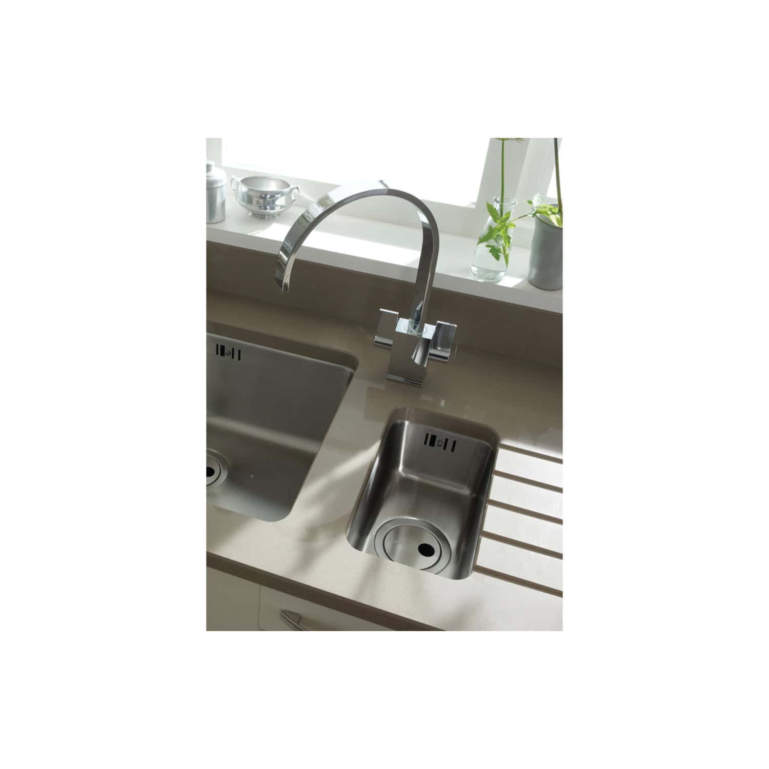 Sleek stainless steel kitchen sink and modern chrome faucet in a contemporary kitchen setup. Featuring double sinks, fresh greenery, and stylish accessories for a functional and elegant kitchen design.