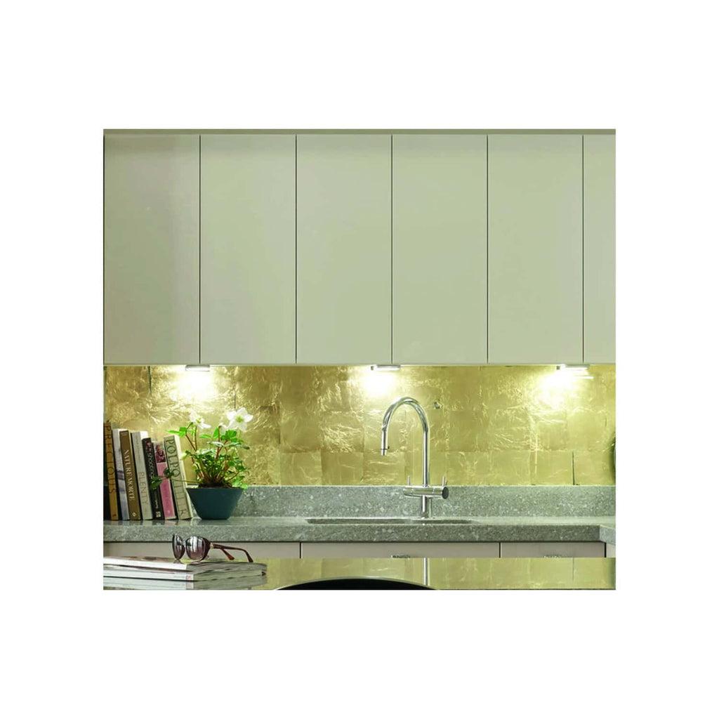 Sleek modern kitchen featuring upper cabinets, a gold marble backsplash, a stainless steel sink with a chrome faucet, and a stone countertop with coffee table books and accessories, stylish kitchen design.