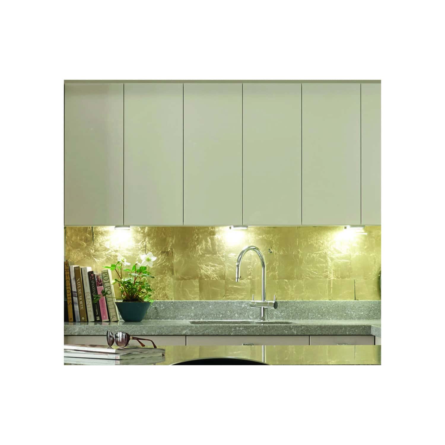 Sleek modern kitchen featuring upper cabinets, a gold marble backsplash, a stainless steel sink with a chrome faucet, and a stone countertop with coffee table books and accessories, stylish kitchen design.