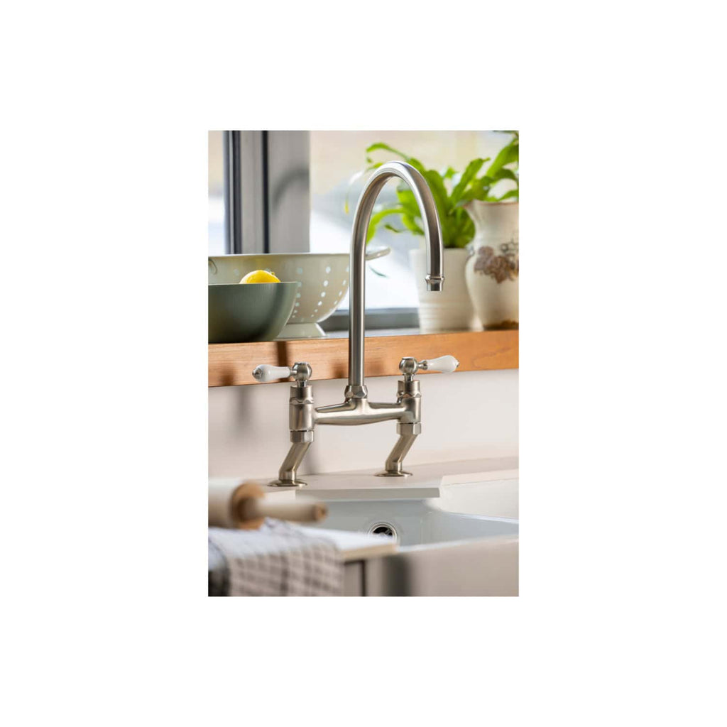 Elegant stainless steel kitchen tap in front of a window with a wooden window sill, surrounded by green potted plants and kitchen utensils, highlighting modern bathroom and kitchen fixtures.