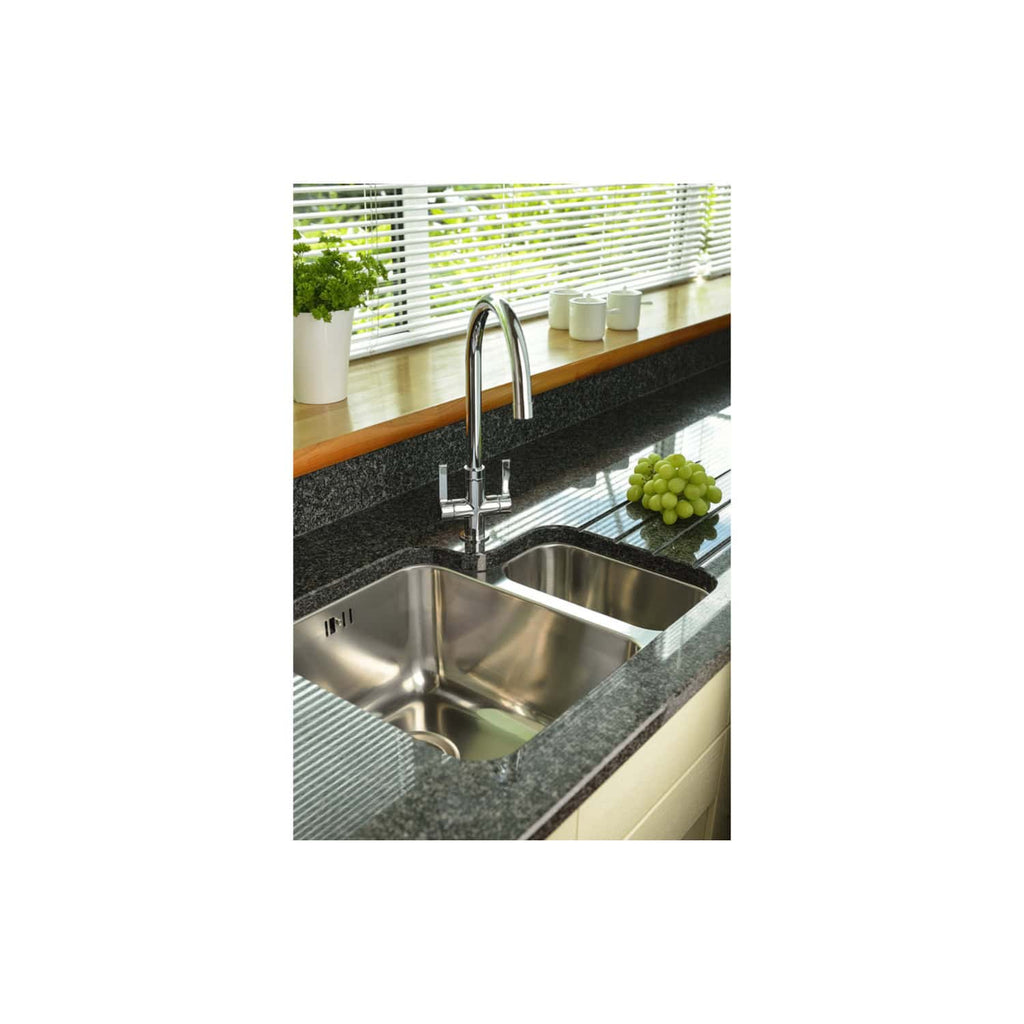 Stainless steel kitchen sink with chrome faucet, black granite countertop, window with blinds, green grapes, and white mugs on wooden windowsill in modern bathroom or kitchen setting.