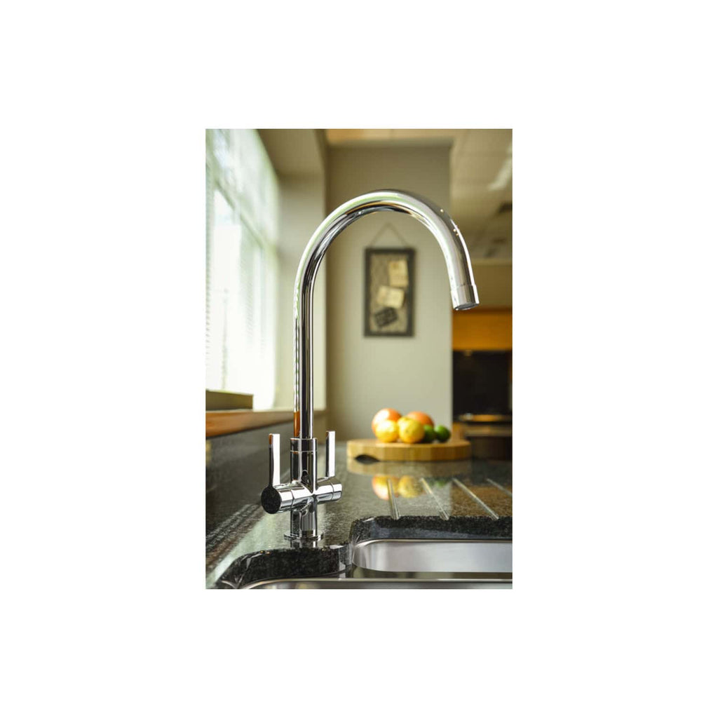 Shiny chrome kitchen tap on black granite sink in bright modern kitchen with natural light and fresh fruits in the background.