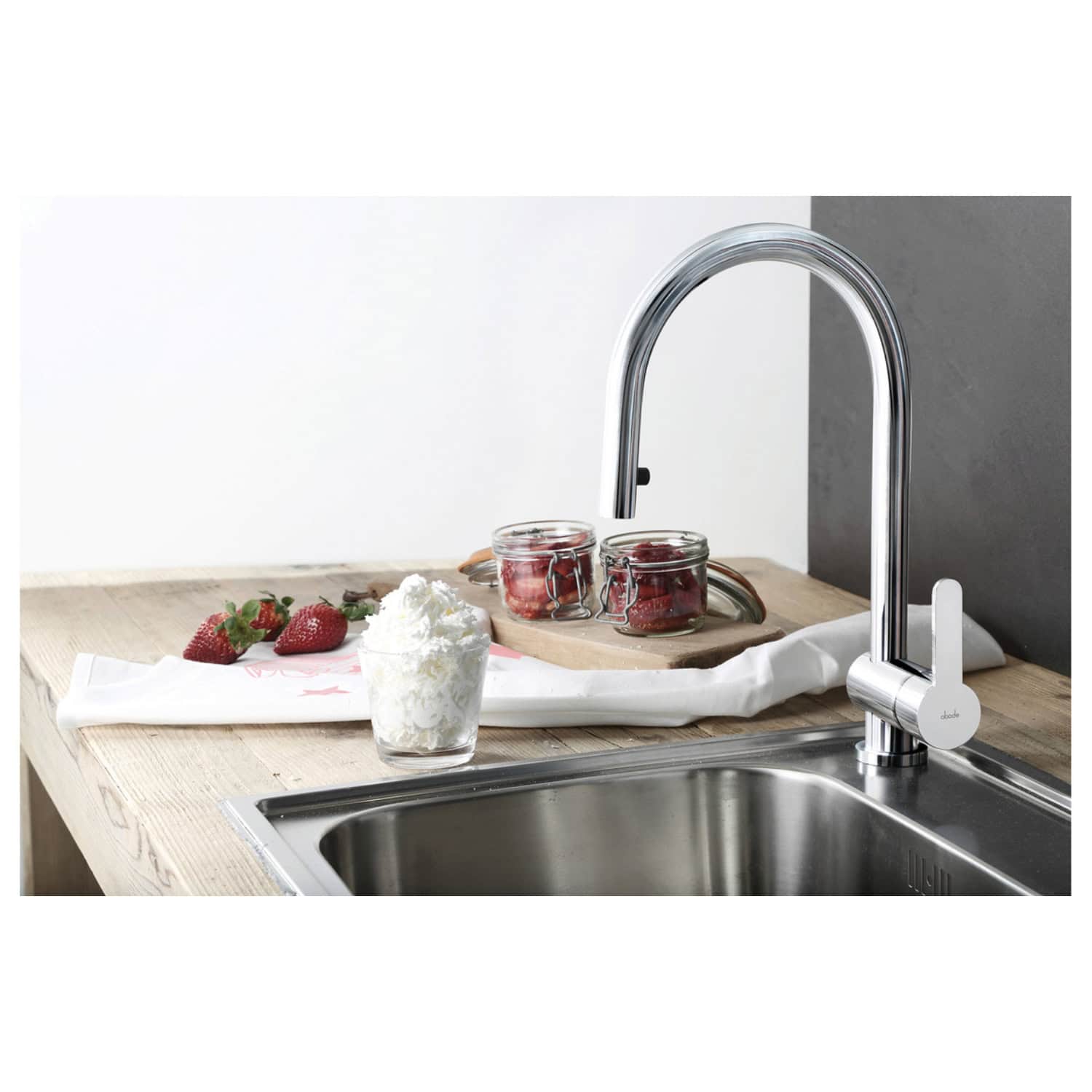 Sleek modern kitchen sink with a high-arc chrome faucet, featuring fresh strawberries, jars of strawberries, and whipped cream on a wooden countertop, ideal for stylish kitchen upgrades.
