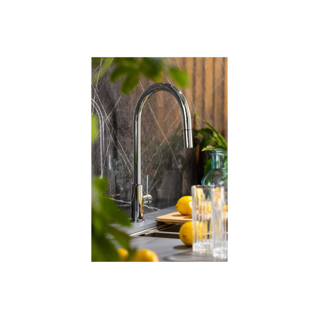 Polished chrome kitchen tap with a high arc spout, installed on a kitchen sink with a dark marble backsplash, surrounded by fresh lemons, glassware, and green plants, creating a modern and stylish kitchen scene.