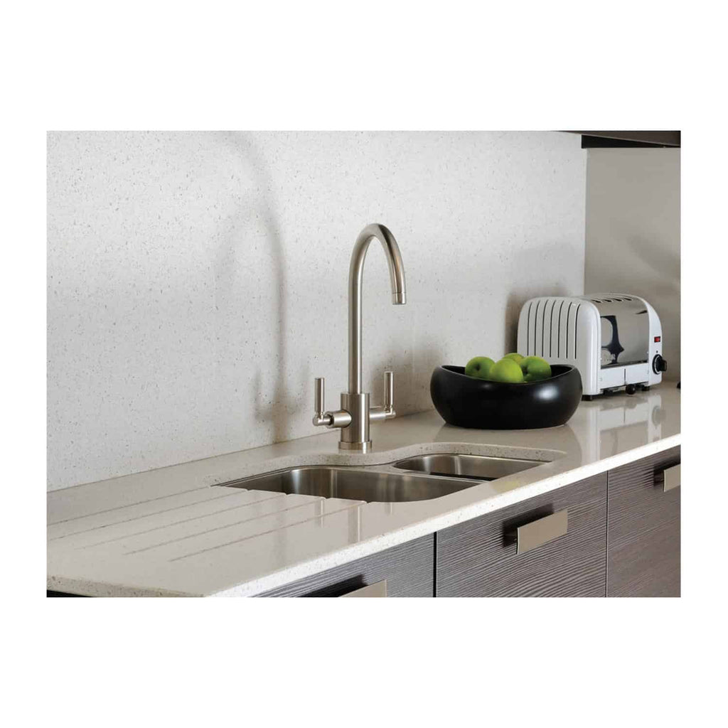 Shiny stainless steel kitchen sink with modern curved faucet, black fruit bowl with green apples, and compact white toaster on light beige countertop in contemporary bathroom setting.
