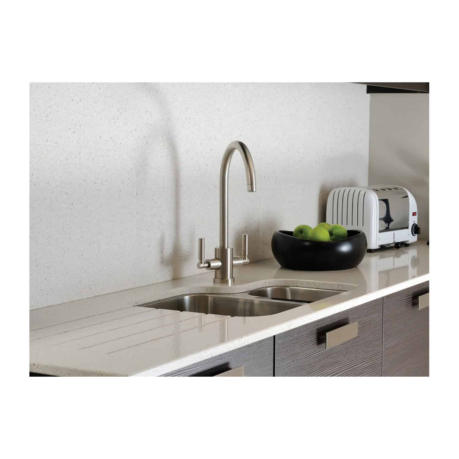 Shiny stainless steel kitchen sink with modern curved faucet, black fruit bowl with green apples, and compact white toaster on light beige countertop in contemporary bathroom setting.