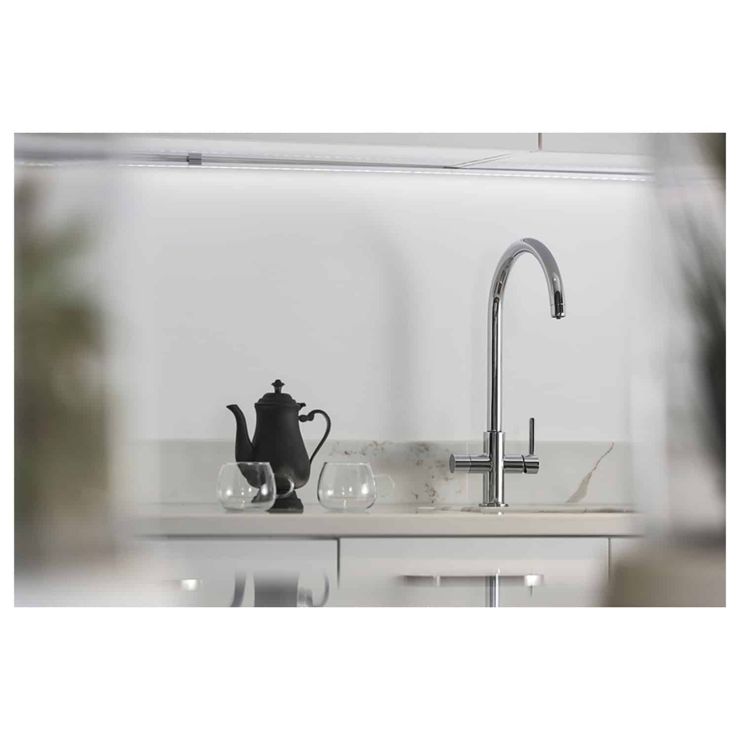 Shiny chrome kitchen faucet mounted on a white marble countertop with a black teapot and glass cups, modern and sleek kitchen sink setup.