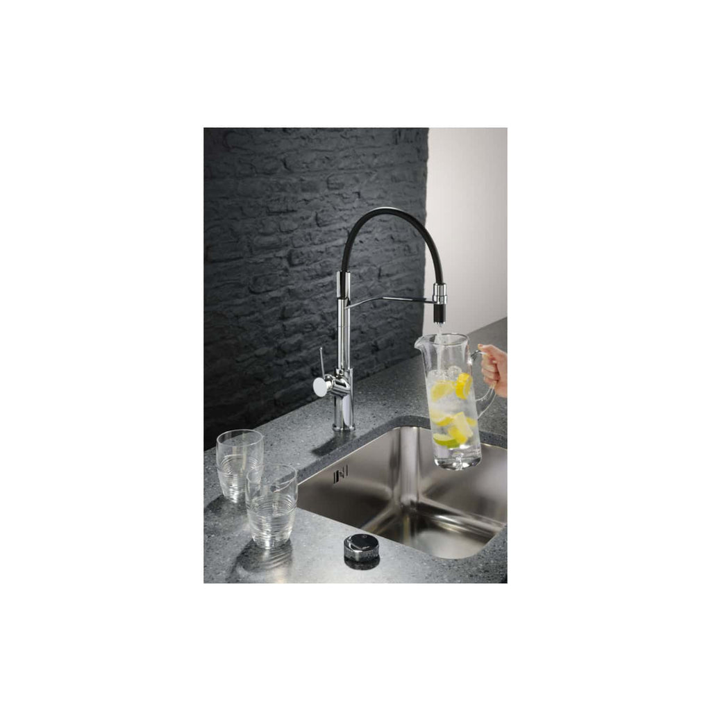 Shiny modern kitchen tap with a black flexible spout over a stainless steel sink, filling a glass pitcher with lemon-infused water, surrounded by clear glasses on a grey worktop against a textured stone wall.