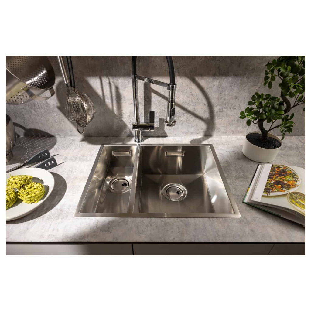 Stainless steel kitchen sink with dual compartments, modern chrome faucet, and surrounding kitchen accessories including utensils, a potted plant, and a cookbook, showcasing premium Bubly Bathrooms kitchen design.