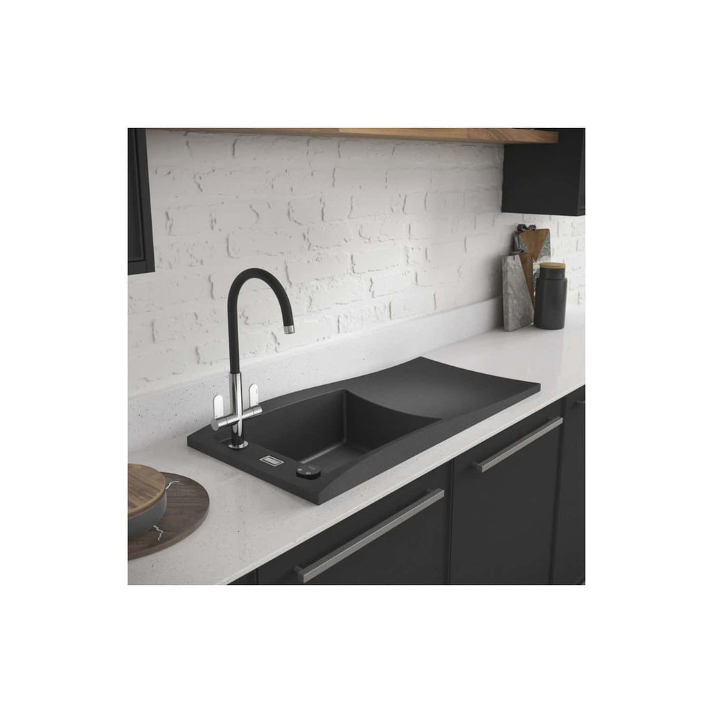 Black kitchen sink with modern chrome faucet in a contemporary kitchen setup with white speckled countertop and brick wall backsplash.