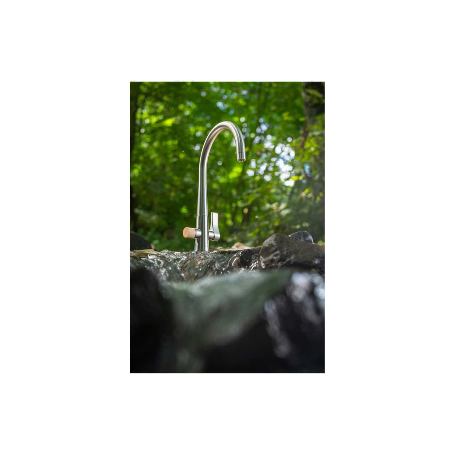 Clean outdoor stainless steel garden tap with curved spout on natural stone, surrounded by lush green trees and foliage, ideal for eco-friendly outdoor bathroom or garden design, sleek modern style.