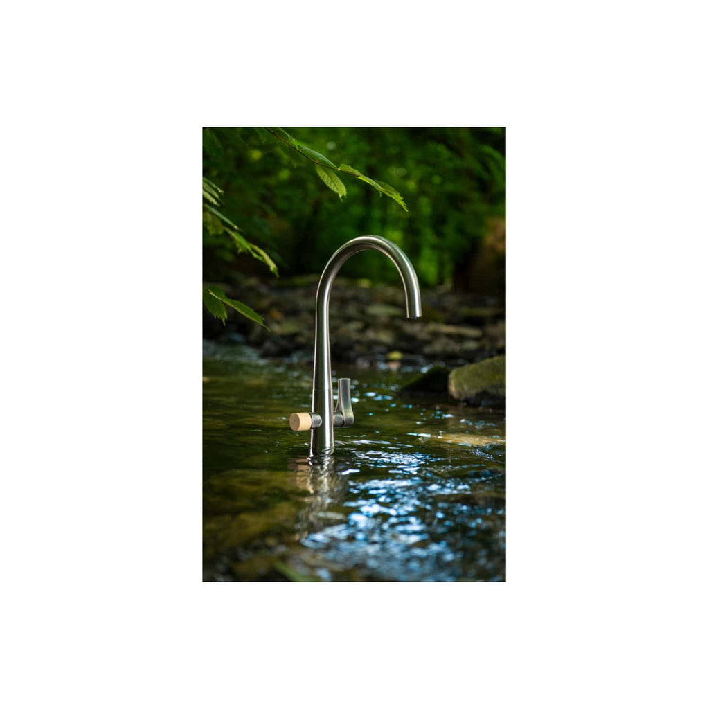 Modern outdoor stainless steel garden water tap installed in a natural setting, surrounded by greenery and flowing water, ideal for eco-friendly and sustainable bathroom and garden solutions.