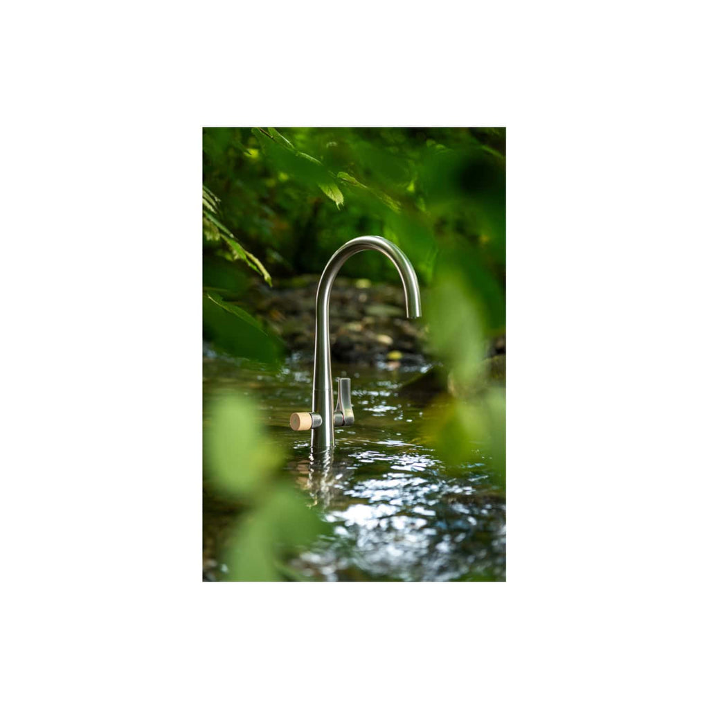 Stainless steel kitchen tap installed in a peaceful garden stream surrounded by green foliage.
