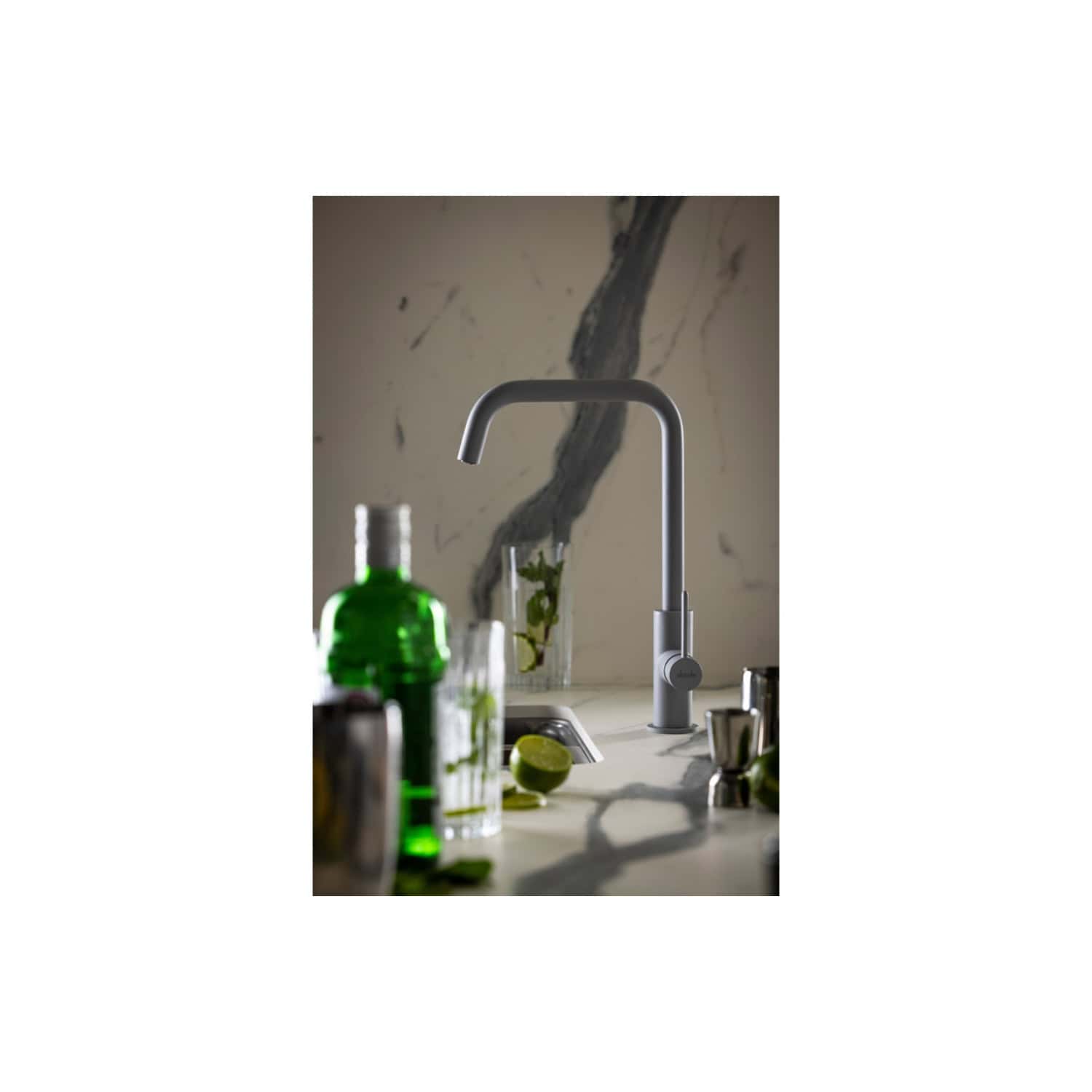 Sleek modern kitchen faucet with a minimalist design, mounted on a marble countertop with various drink bottles and lime slices, showcasing contemporary bathroom and kitchen fixtures.