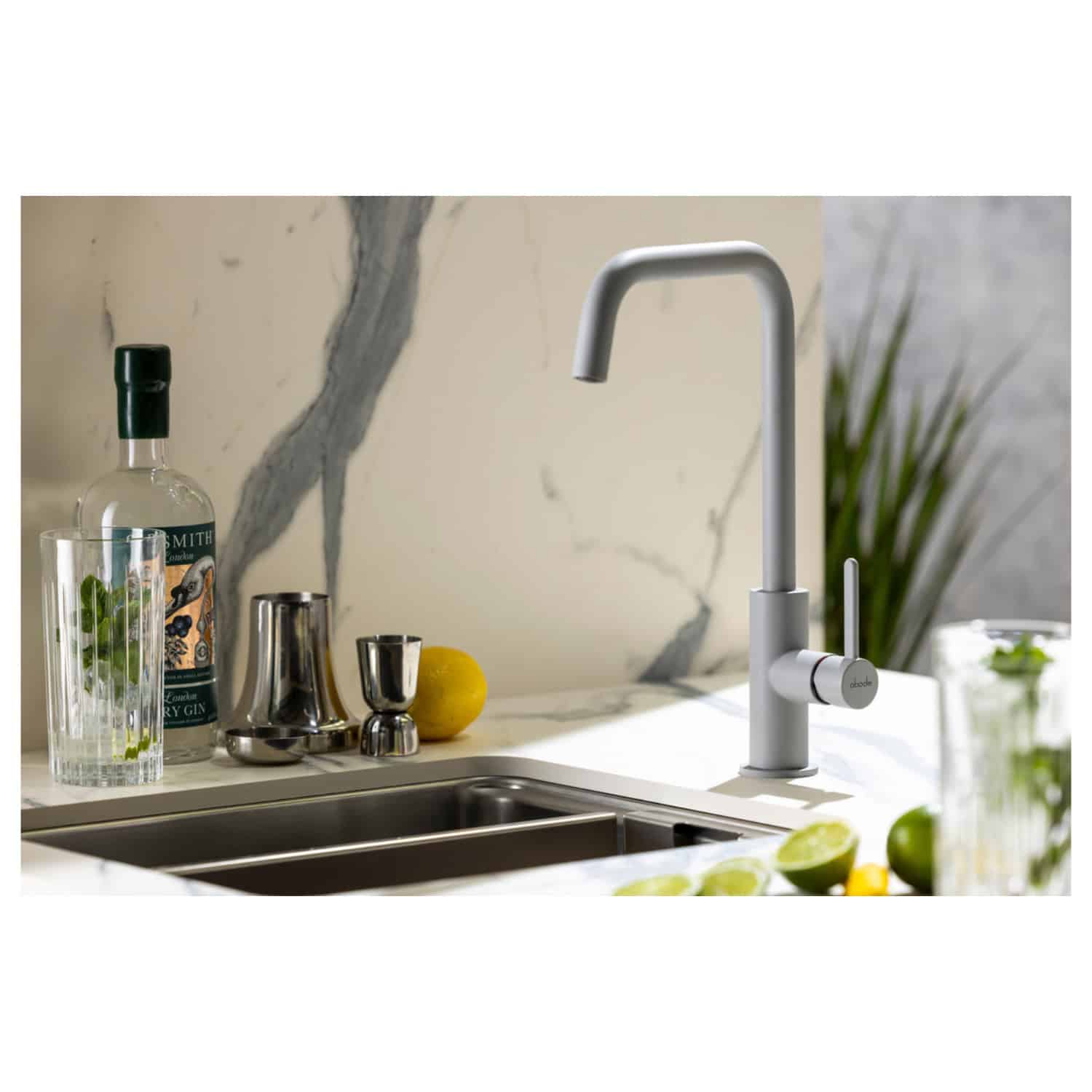 Sleek modern kitchen sink with white minimalist tap, surrounded by fresh lemons, limes, and stylish barware, set against a luxurious marble backsplash. Perfect for contemporary kitchen design and eco-friendly living.