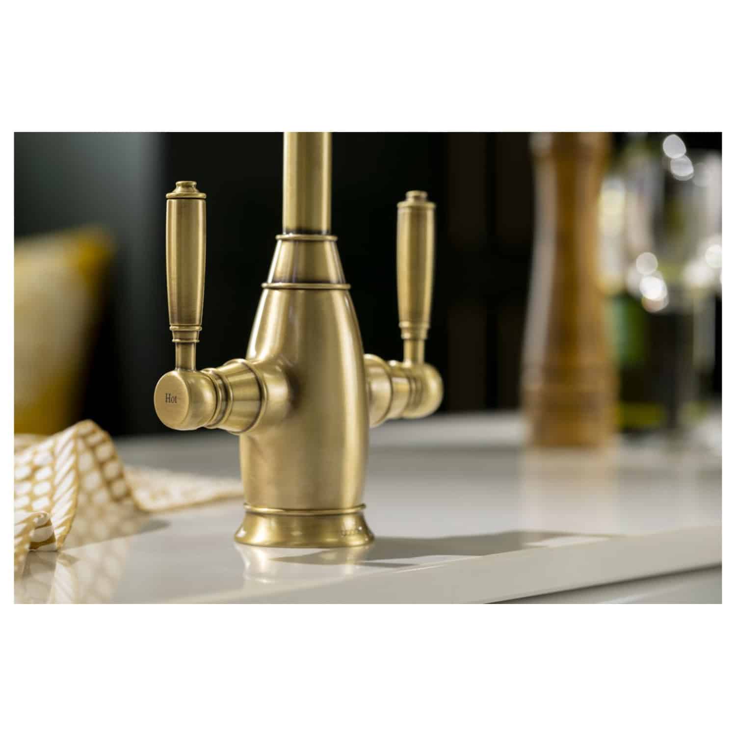 Polished gold dual-handle kitchen tap with traditional design, featuring hot water indicator, mounted on a white countertop in a modern bathroom or kitchen setting. Elegant fixture enhancing luxury interiors.