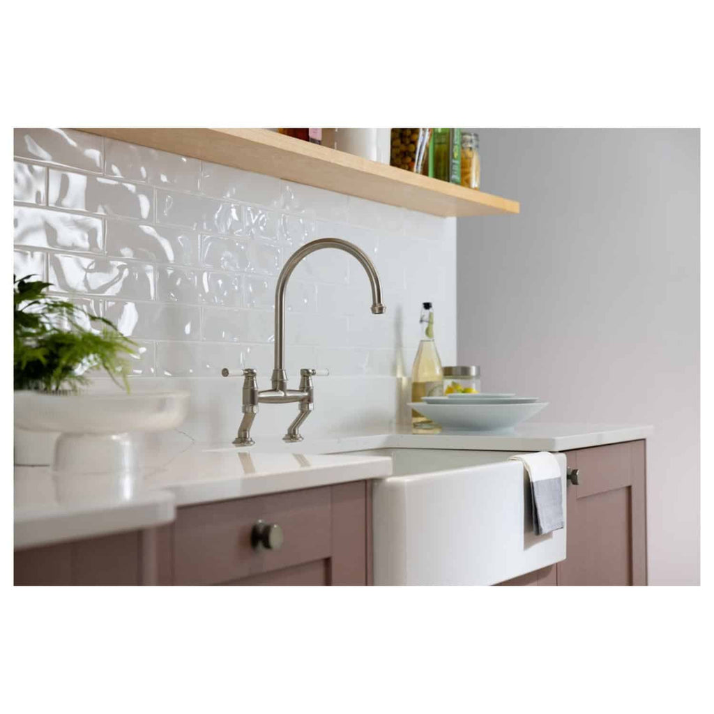 Sleek stainless steel kitchen tap with traditional design, installed over a vintage farmhouse style sink in a modern kitchen with white subway tile splashback and wooden accents.
