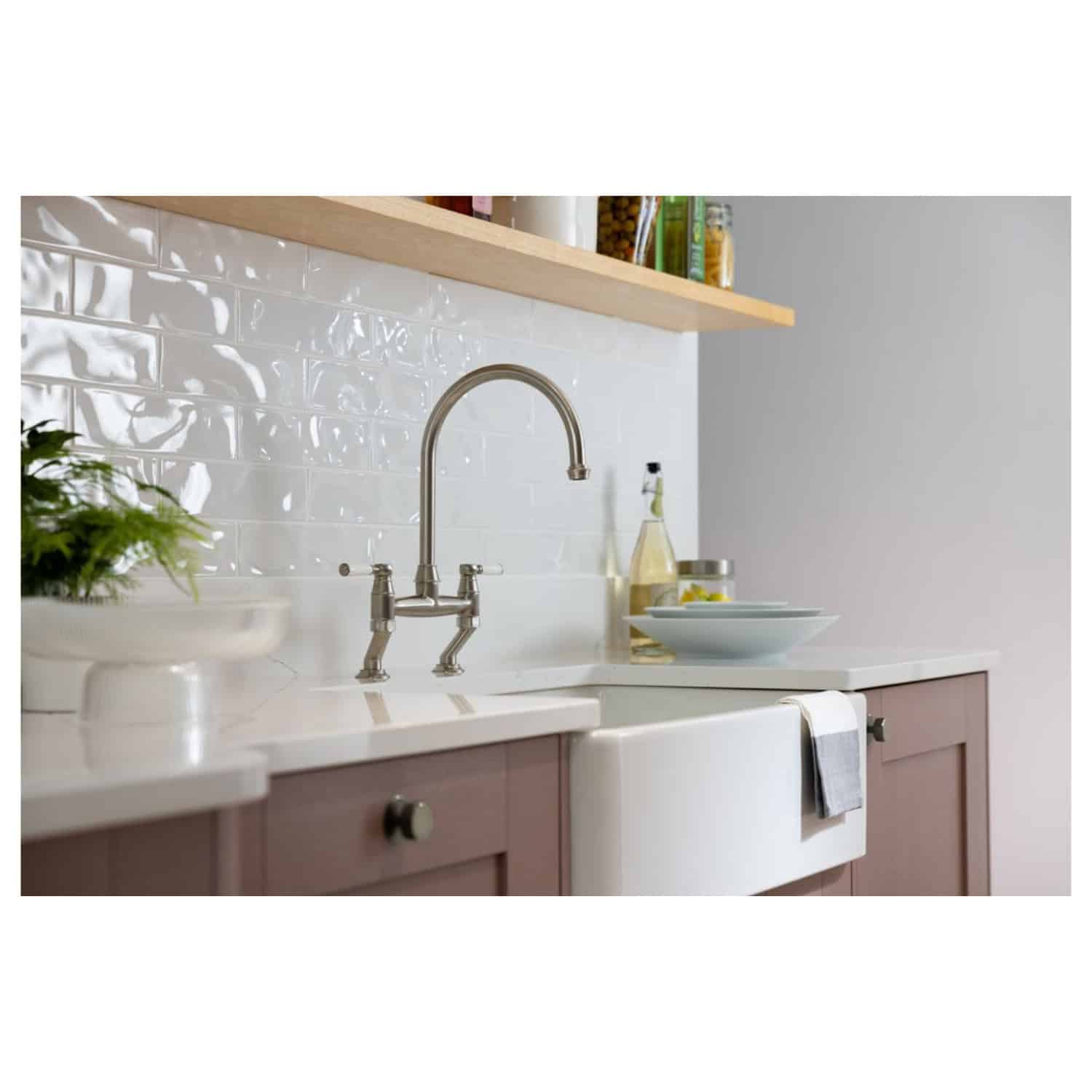Sleek stainless steel kitchen tap with traditional design, installed over a vintage farmhouse style sink in a modern kitchen with white subway tile splashback and wooden accents.