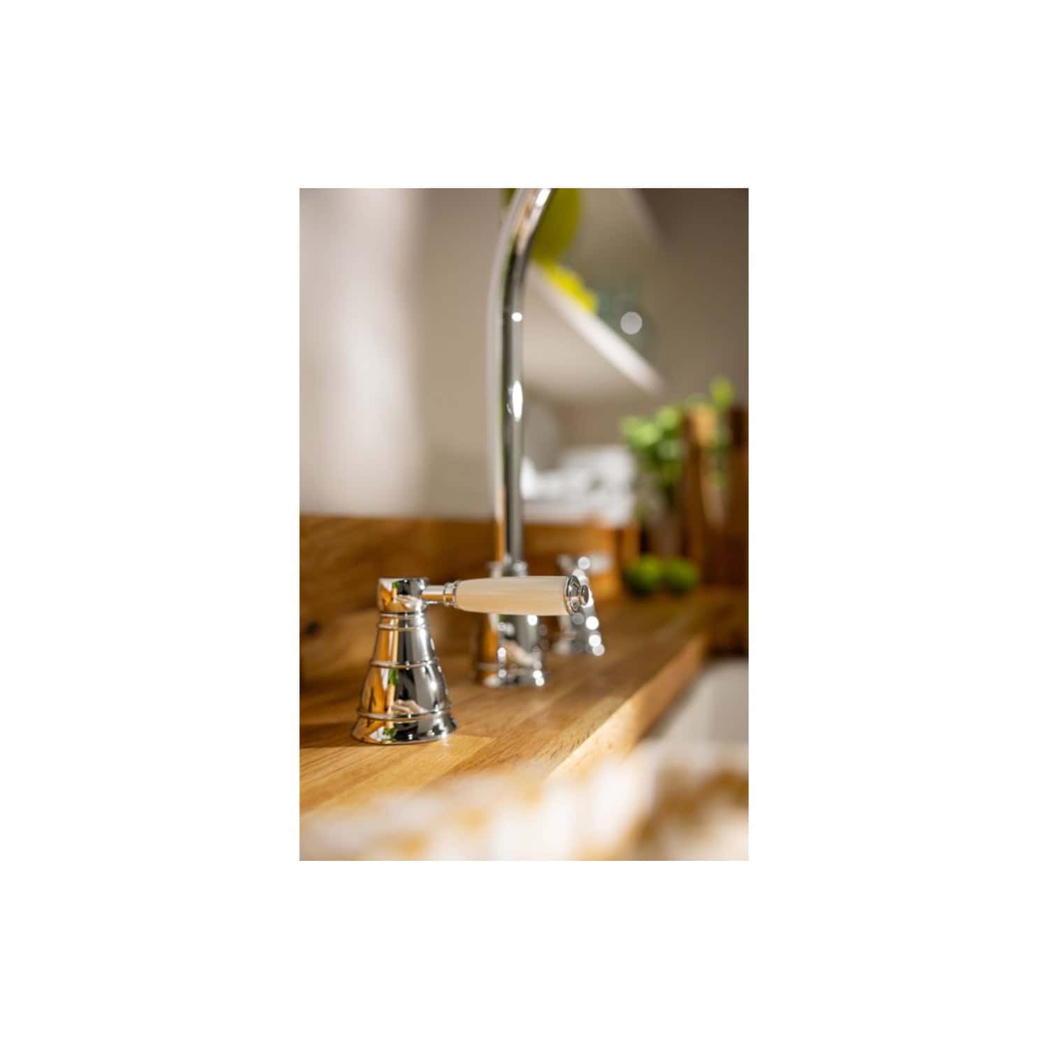 Shabby chic kitchen sink tap with cream handles, polished chrome finish, mounted on a rustic wooden countertop with a blurred background of kitchen decor and greenery.