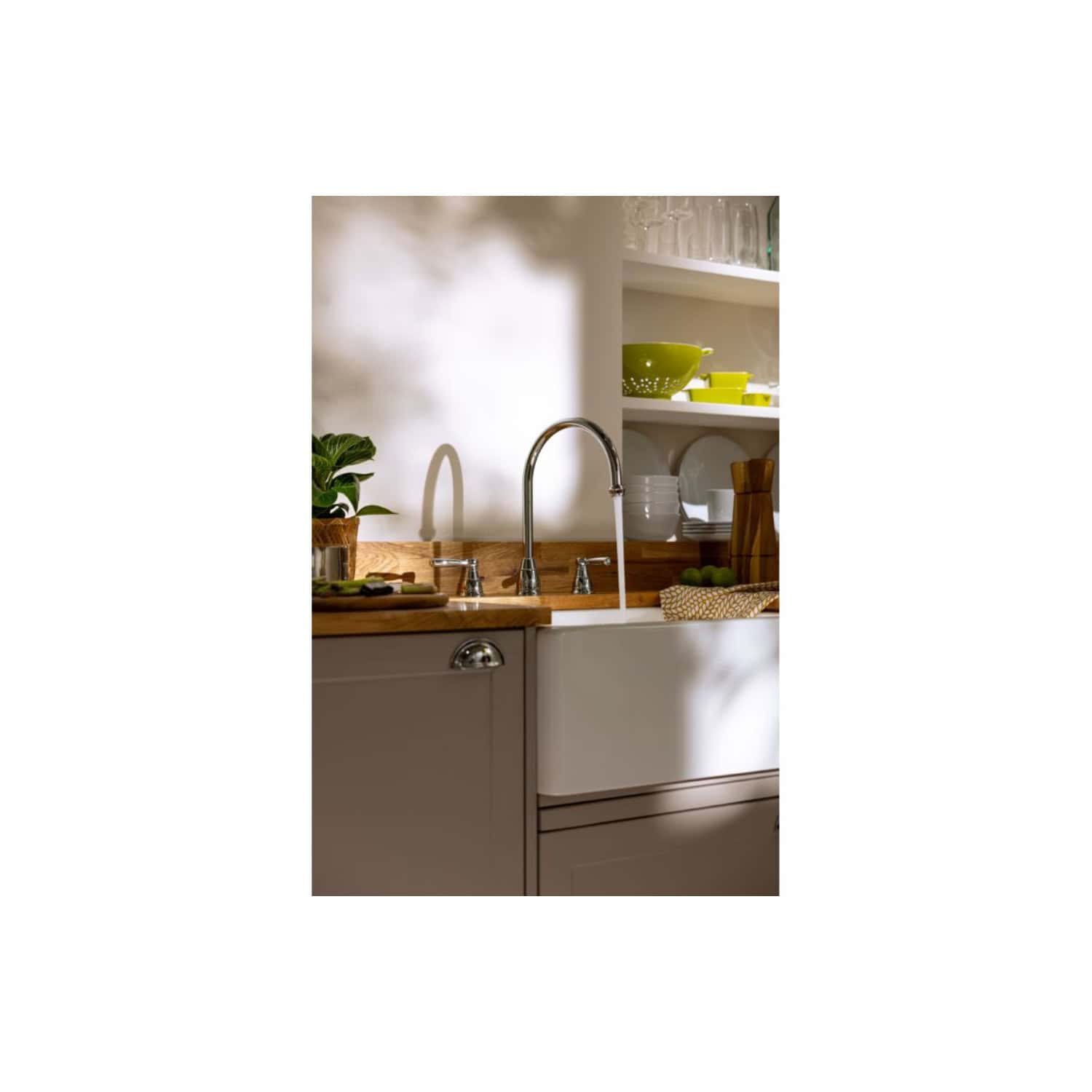Bright modern kitchen with farmhouse sink, wooden countertop, open shelving with colourful dishes, and fresh green plants, showcasing stylish and functional kitchen design.