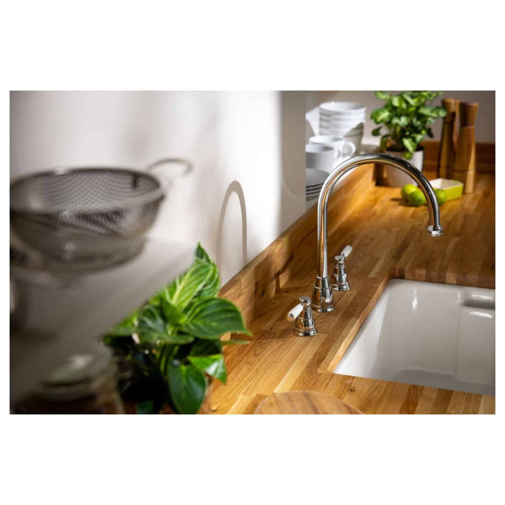 Sleek kitchen sink with polished chrome taps and wooden countertop, surrounded by modern tableware, green plants, and kitchen accessories, showcasing stylish and functional Bubly Bathrooms kitchen design.