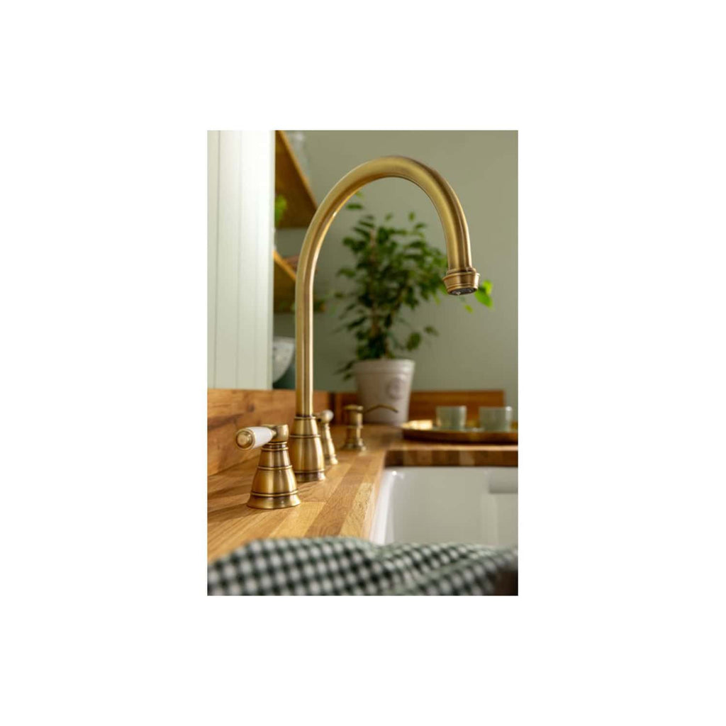 Brass kitchen sink tap with a high-arc spout and vintage design, installed on a wooden countertop in a modern, stylish kitchen with green plants and minimal decor.
